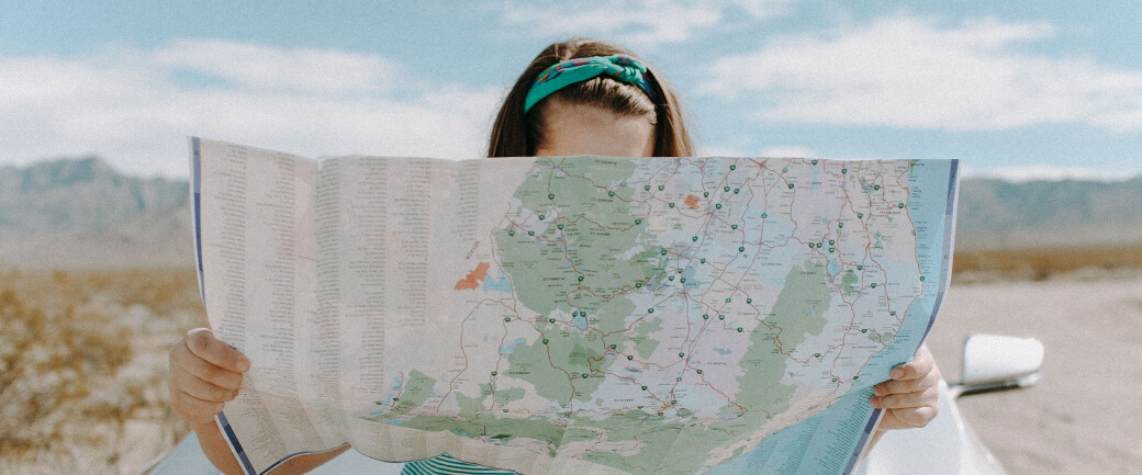 a woman looks at a map while standing in front of her car; insights