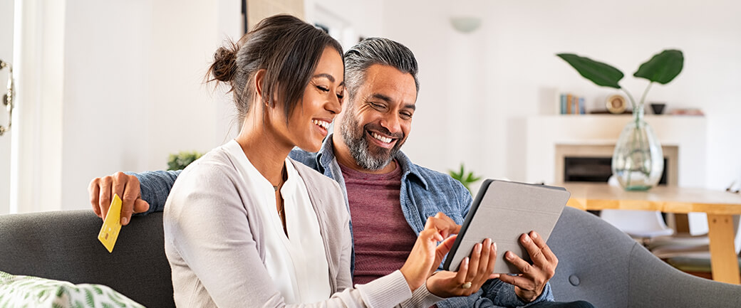 A man and a woman sit on a sofa while shopping on a tablet device