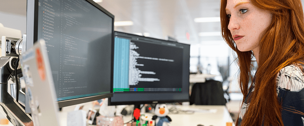 a woman works at a desk with two monitors and a laptop