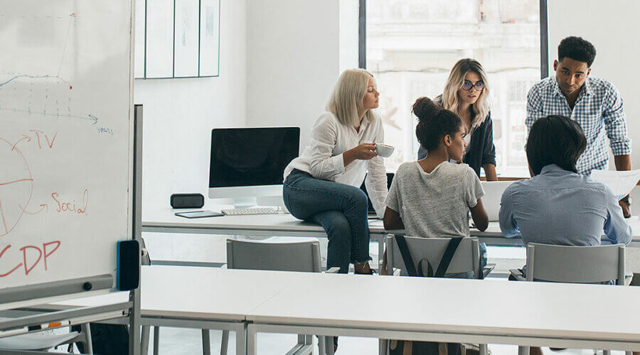 A group of people sit at a conference table in a room with a whiteboard