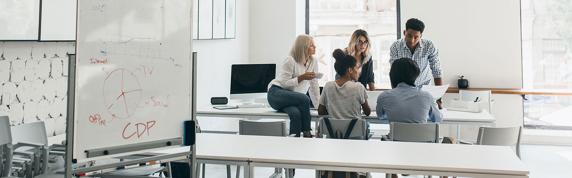 A group of people sit at a conference table in a room with a whiteboard