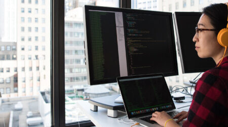 A person works at a computer station and looks out the window pensively